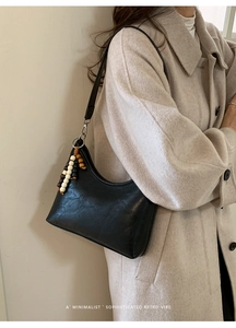 Minimalist black crescent bag with vintage beaded tassel shown on a stylish coat