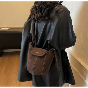 Détail du sac seau en daim marron foncé avec surpiqûres blanches et nœud décoratif