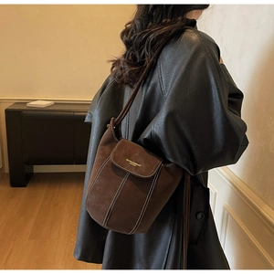 Détail du sac seau en daim marron foncé avec coutures blanches contrastées et logo