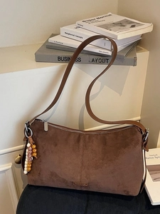 Sac bandoulière marron en daim style dumpling avec pompon bohème sur fond minimaliste