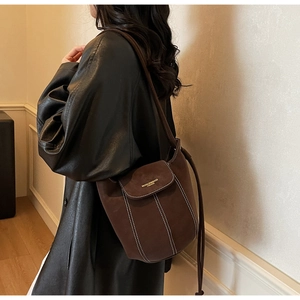 Détail du sac seau en daim marron foncé avec surpiqûres contrastées et logo doré
