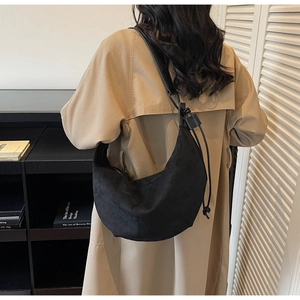 Detail of minimalist black suede crescent bag with adjustable knotted strap on a trench coat
