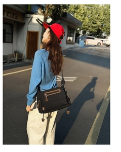 Close-up of black crossbody bag with multiple zipper pockets and heart charm in golden hour light