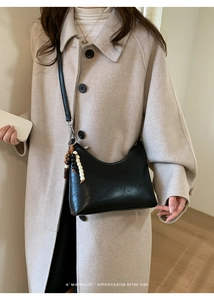 Detail of minimalist black leather bucket bag with retro wooden bead charm on beige coat