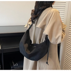 Detail of minimalist black suede hobo bag with drawstring on a trench coat model