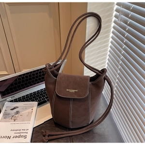 Détail du sac seau en daim marron avec surpiqûres blanches et bandoulière à nœud minimaliste