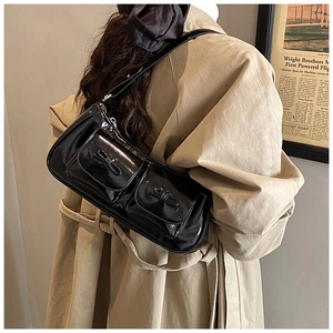 Detail of black glossy shoulder bag featuring dual front pockets with chic ribbon bows