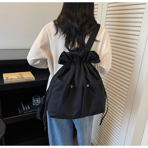 Detail of black drawstring bucket bag with ruffles and front pockets on a model