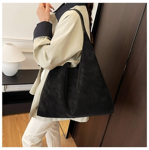 Side view of a large black matte leather tote bag with a wide shoulder strap for women