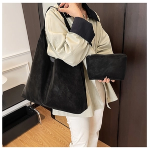 Detail view of large matte black tote bag and matching clutch set on woman shoulder