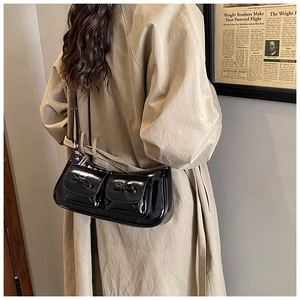 Close-up of black patent leather shoulder bag with double pockets and bow details