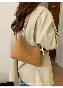 Detail of tan crescent shoulder bag with wooden bead charm and silver metal buckle