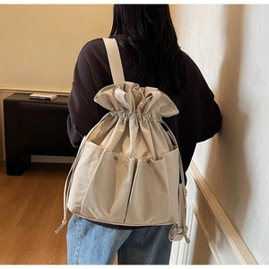 Detail of off-white canvas bucket backpack with drawstring closure and multiple pockets