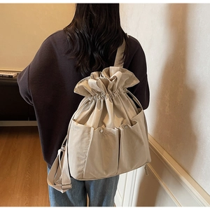 Detail view of beige canvas bucket backpack featuring drawstring closure and three front pockets