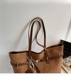 Close-up of brown textured leather tote bag with metal buckle and plush bear pendant