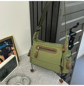 Close-up of green utility messenger bag featuring leather pullers and heart-shaped pendant