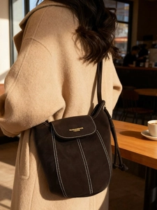 Sac seau minimaliste en daim marron foncé avec surpiqûres contrastées sur modèle