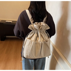 Detail of beige bucket backpack with drawstring closure and functional pockets on a model