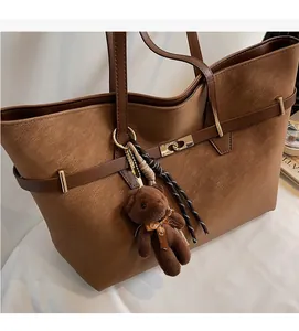 Close-up of brown suede tote bag with golden metal buckle and brown teddy bear charm