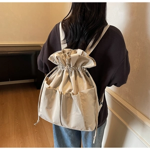 Close-up of beige drawstring bucket backpack with large front pockets on a model