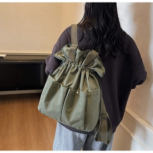 Detail view of olive green drawstring bucket backpack featuring dual front utility pockets