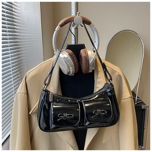 Detail view of black glossy baguette bag featuring bow-knot pockets and shoulder strap