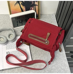 Detail of red nylon messenger bag with brown leather zipper pull on gray felt background