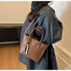 Detail view of deep brown tote bag with FASHION&BAGS logo and beaded accessory charm