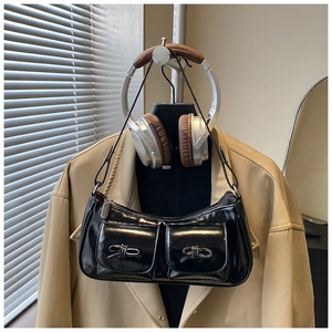 Detail of black patent leather baguette bag with dual front pockets and silver bows