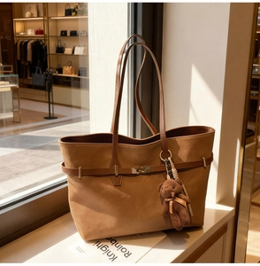 Detailed close-up of brown suede tote bag with belt buckle clasp and bear charm accessory