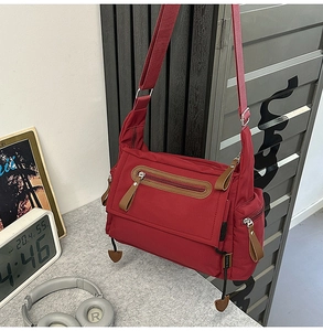 Detail view of the multi-zipper compartments and nylon texture on the red messenger bag