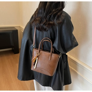 Detail of vintage brown leather bucket bag featuring bohemian beaded pendant and top handles