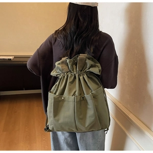 Detail view of army green canvas bucket backpack with drawstring closure and dual front pockets