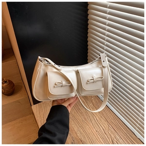 Detail of cream baguette bag with bow accents and pockets against window blinds