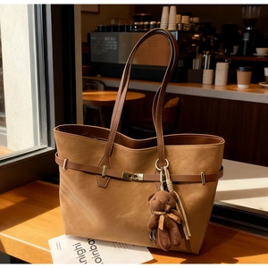 Detailed view of brown tote bag with metal buckle, tassel, and cute bear charm pendant