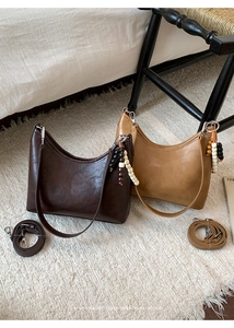 Detail of minimalist bucket bags in caramel and camel leather with beaded charms
