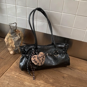 Détail d'un sac à bandoulière en cuir noir brillant avec boucle et breloque léopard