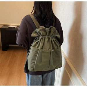 Detail view of military green canvas bucket backpack with drawstring and metal button pockets