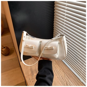 Close-up of white glossy patent leather baguette bag with dual bow-knot flap pockets