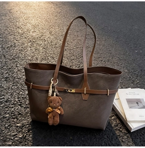 Detail of a dark brown faux leather tote bag with gold lock and plush bear charm