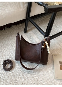 Deep brown glossy bucket bag with wooden bead charm on soft white fleece carpet