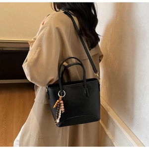 Detail of black PU leather bucket bag with colorful bead charm on a long trench coat