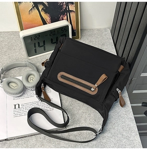 Detailed view of black messenger bag with brown leather zipper pulls on a desk