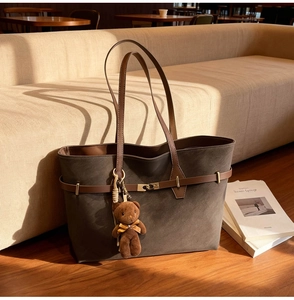 Detail of dark brown suede tote bag with golden buckle and cute plush bear pendant