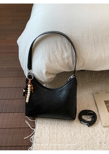 Detail of black semi-circle bucket bag with wooden bead tassel on a white bed