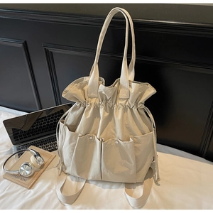 Detail of cream bucket bag showing drawstring closure and functional front utility pockets