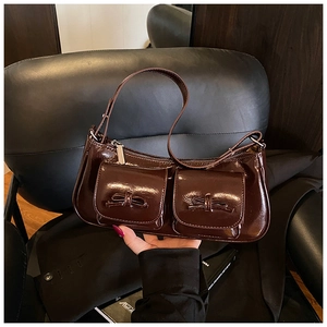 Detailed view of dark brown patent leather baguette bag with dual pockets and bows