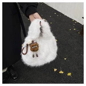 Dettaglio borsa a secchiello in peluche bianca con ciondolo mostro su foglie di ginkgo