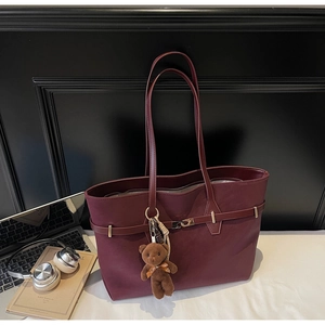 Detail shot of a burgundy tote bag with metal buckle, plush bear charm and work accessories