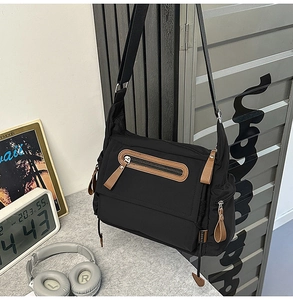 Detail view of black nylon messenger bag featuring brown leather zipper pulls and multiple pockets
